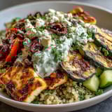 Sliced chicken and halloumi rest over fluffy quinoa in a Healthy Grilled Mediterranean Bowl drizzled with creamy tzatziki sauce.