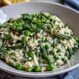 Creamy pea and mint risotto with Parmesan, garnished with fresh herbs and lemon zest for a bright spring dinner party dish.