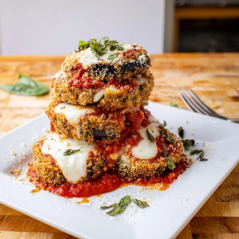 Golden, baked Eggplant Parmesan layers with rich marinara and melted mozzarella, served in a white ceramic baking dish.