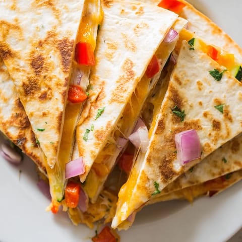 Sliced into wedges, cheesy vegetable quesadillas are served with fresh guacamole and salsa for a classic Mexican dinner.