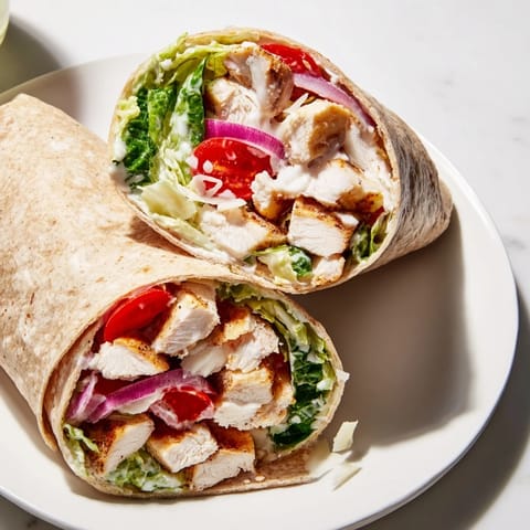 Sliced Chicken Caesar Wrap halves show shaved Parmesan and cherry tomatoes on a clean wooden board.