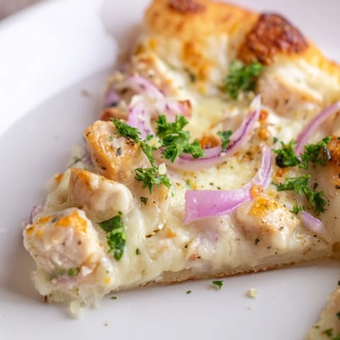 Golden crust Chicken Alfredo Pizza with creamy sauce, tender chicken, and melted cheese on a rustic baking sheet.  