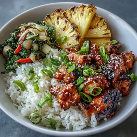 A close-up of a Teriyaki Chicken and Rice Bowl garnished with fresh pineapple chunks and sliced scallions.