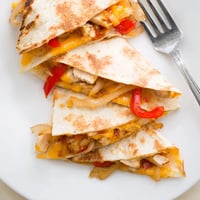 Golden-brown Chicken Quesadilla wedges, filled with grilled chicken, sautéed peppers, and melty cheese, served with sour cream.