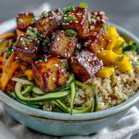 Bright orange spiralized carrots and green zucchini noodles top fluffy quinoa in this vibrant Easy Teriyaki Quinoa Bowl with crispy baked tofu.