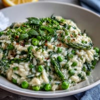 Creamy pea and mint risotto with Parmesan, garnished with fresh herbs and lemon zest for a bright spring dinner party dish.